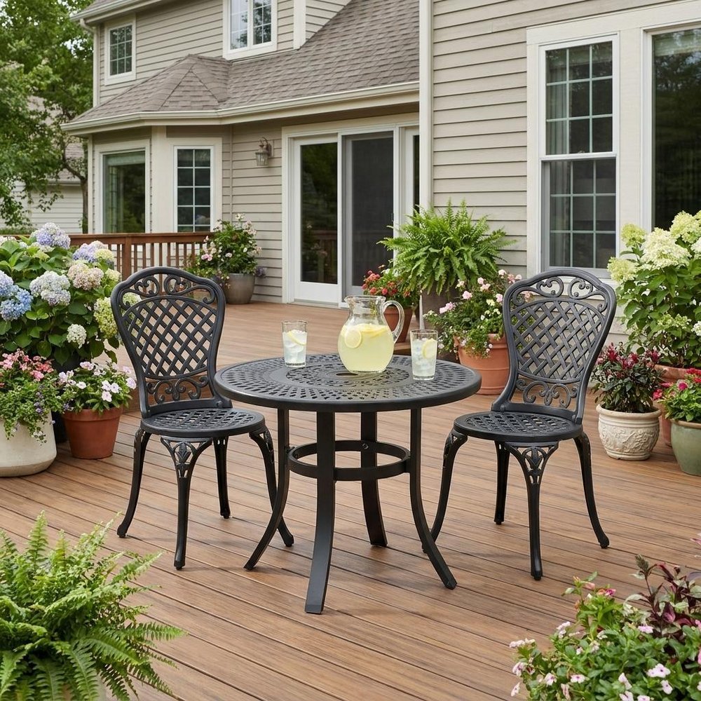 24" Black Rounded Metal Outdoor Bistro Table with Umbrella Hole shown outdoors on a patio with greenery.