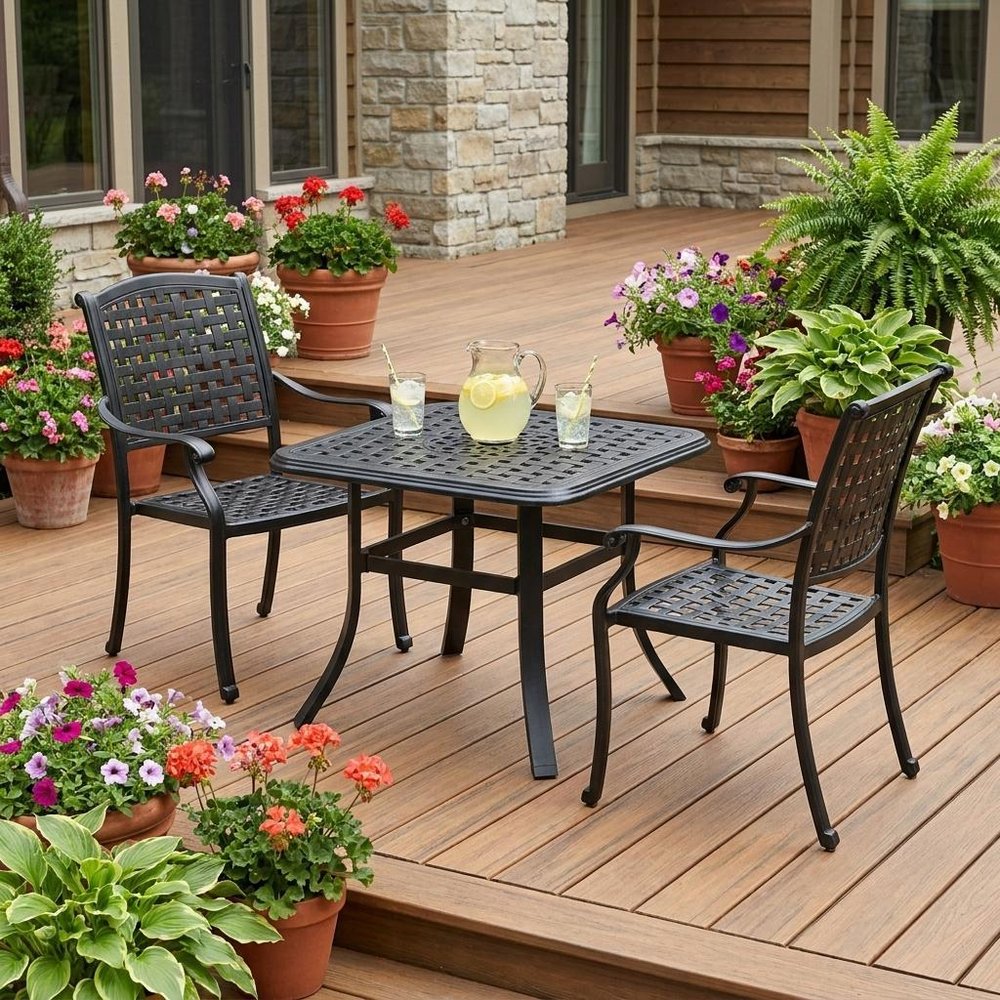 24" Black Square Metal Outdoor Bistro Table with Umbrella Hole shown outdoors on a patio with greenery.