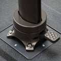 Close-up of a dark bronze metal umbrella base with a diamond-patterned foot pedal on a textured black surface.