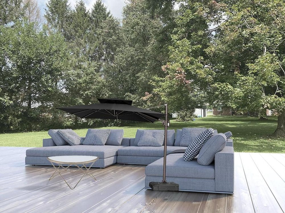 11' Black Polyester Round Tilt Cantilever Patio Umbrella with Stand styled in a furnished interior with a gray wall on a tiled floor.