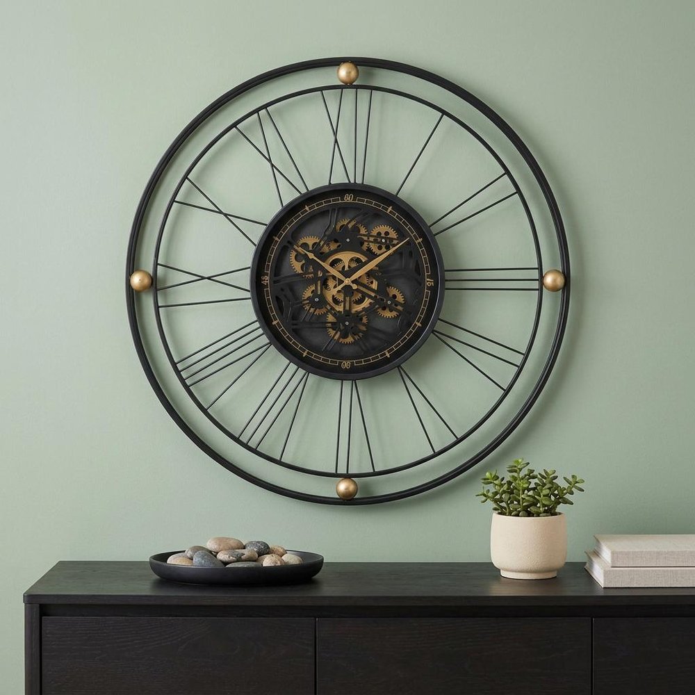32" Circle Black and Gold Metal and Glass Analog Exposed Gear Wall Clock shown outdoors on an outdoor setting with greenery.