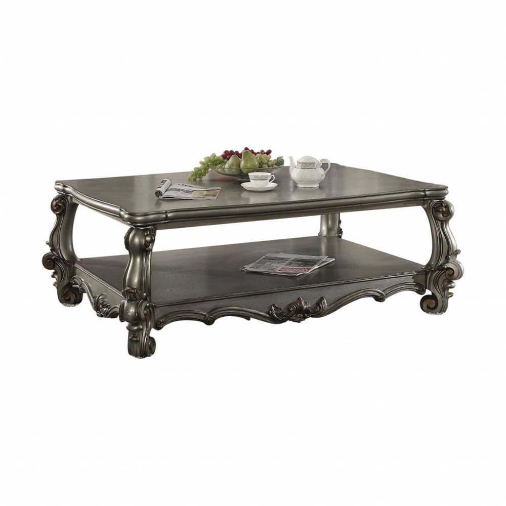 A gray wood and polyresin coffee table with a shelf, featuring ornate carvings and a white background.