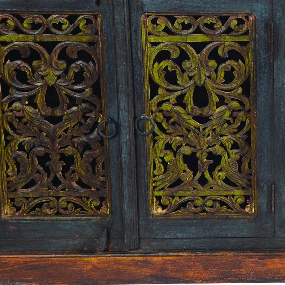 Close-up of a dark blue and green solid wood buffet table with intricately carved doors and ring pulls.