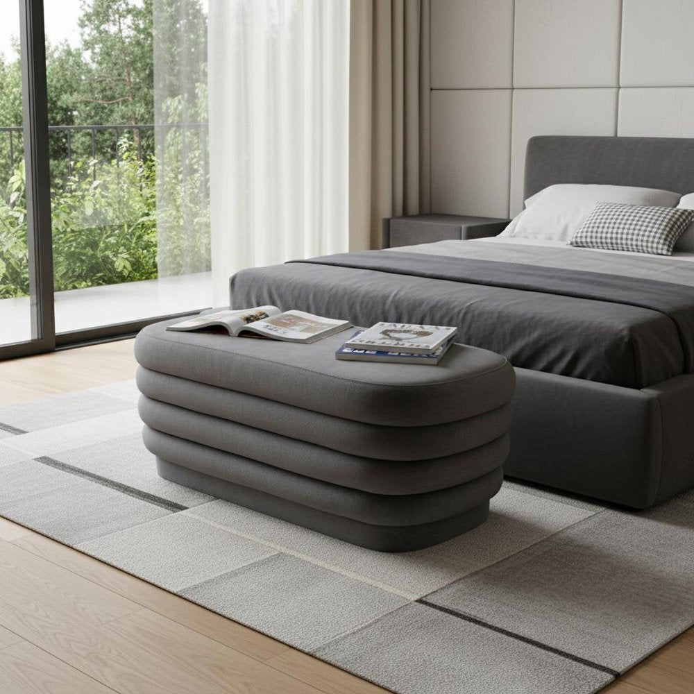 44" Gray Velvet Tufted Oval Ottoman styled in a furnished interior with a light gray wall on a tiled floor.