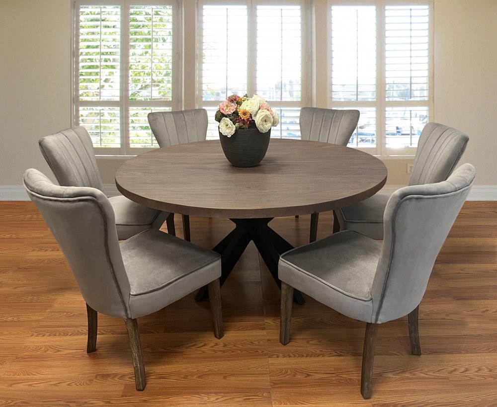 Round gray wood dining table with six gray velvet chairs in a room with white shutters and wood floors.