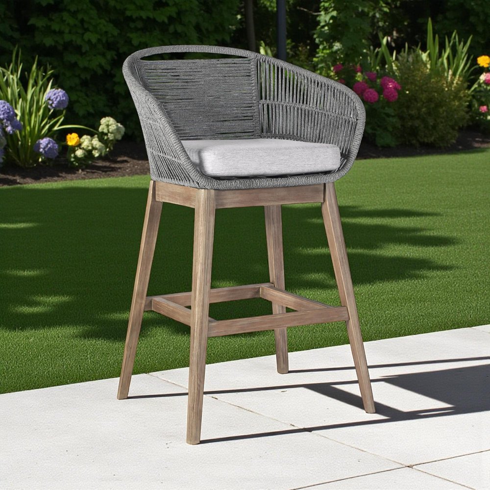 43" Gray Solid Wood Low back Outdoor Bar Height chair with Footrest shown outdoors on a patio with greenery.