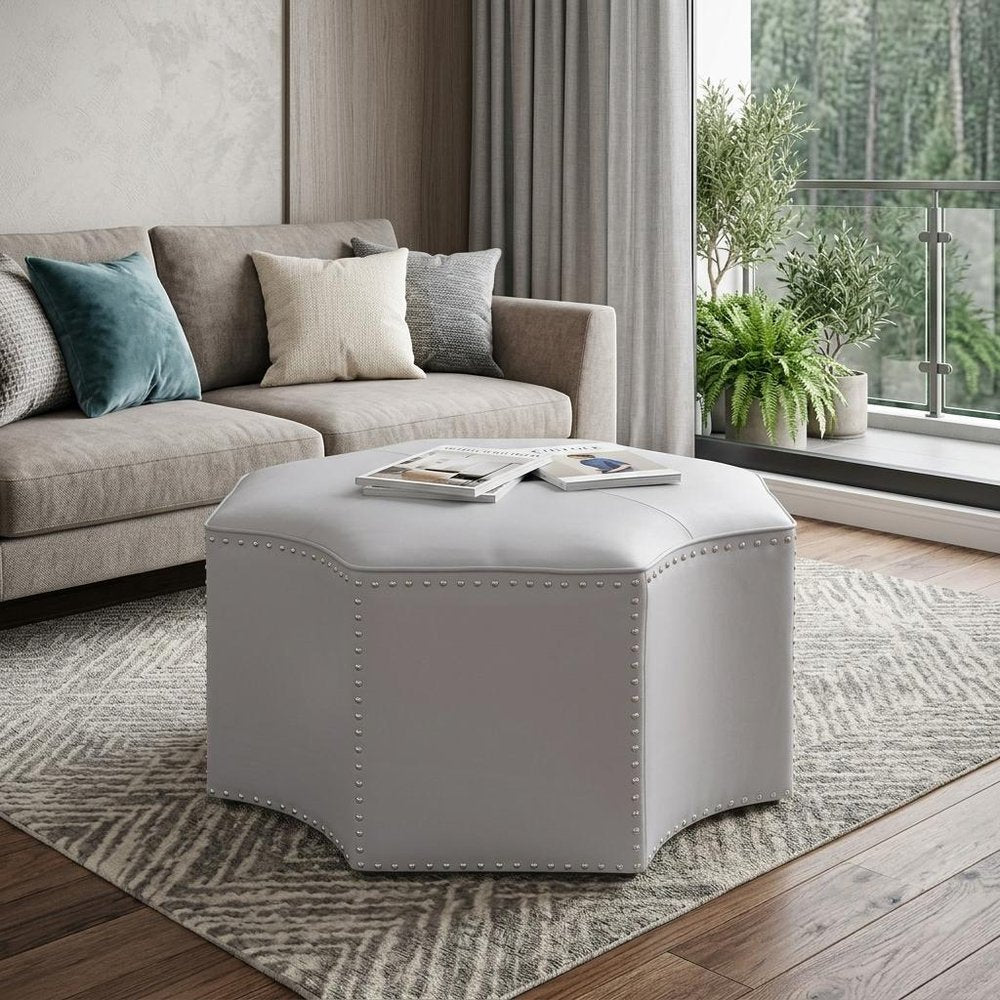 33" Silver Faux Leather Tufted Octagonal Cocktail Ottoman styled in a furnished interior with a gray wall on a dark wood floor.