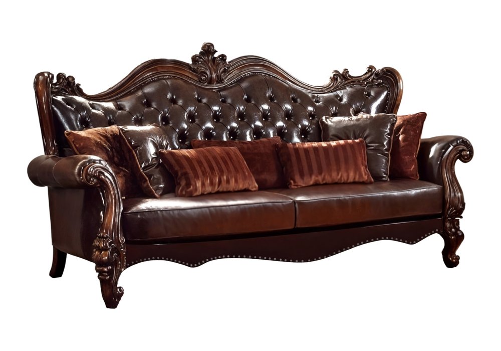 Brown faux leather sofa with tufted back and ornate carved wood legs, featuring brown and striped toss pillows on a white background.