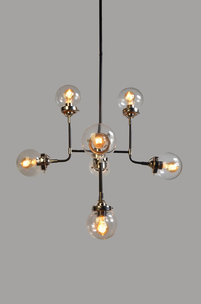 A silver sputnik chandelier with eight clear glass shades and exposed filament bulbs against a gray background.