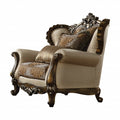 Tan and brown fabric wingback chair with ornate wood trim and damask toss pillows on a white background.