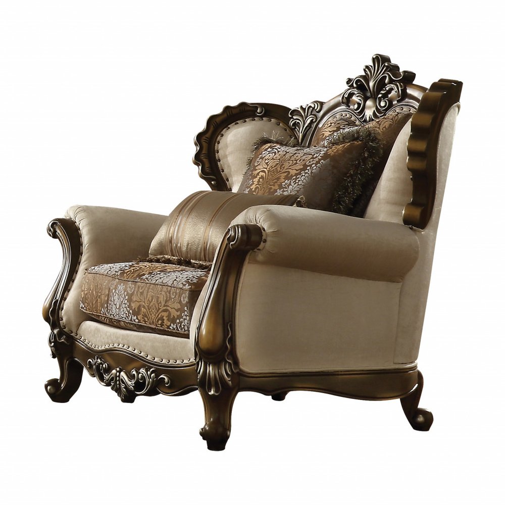 Tan and brown fabric wingback chair with ornate wood trim and damask toss pillows on a white background.