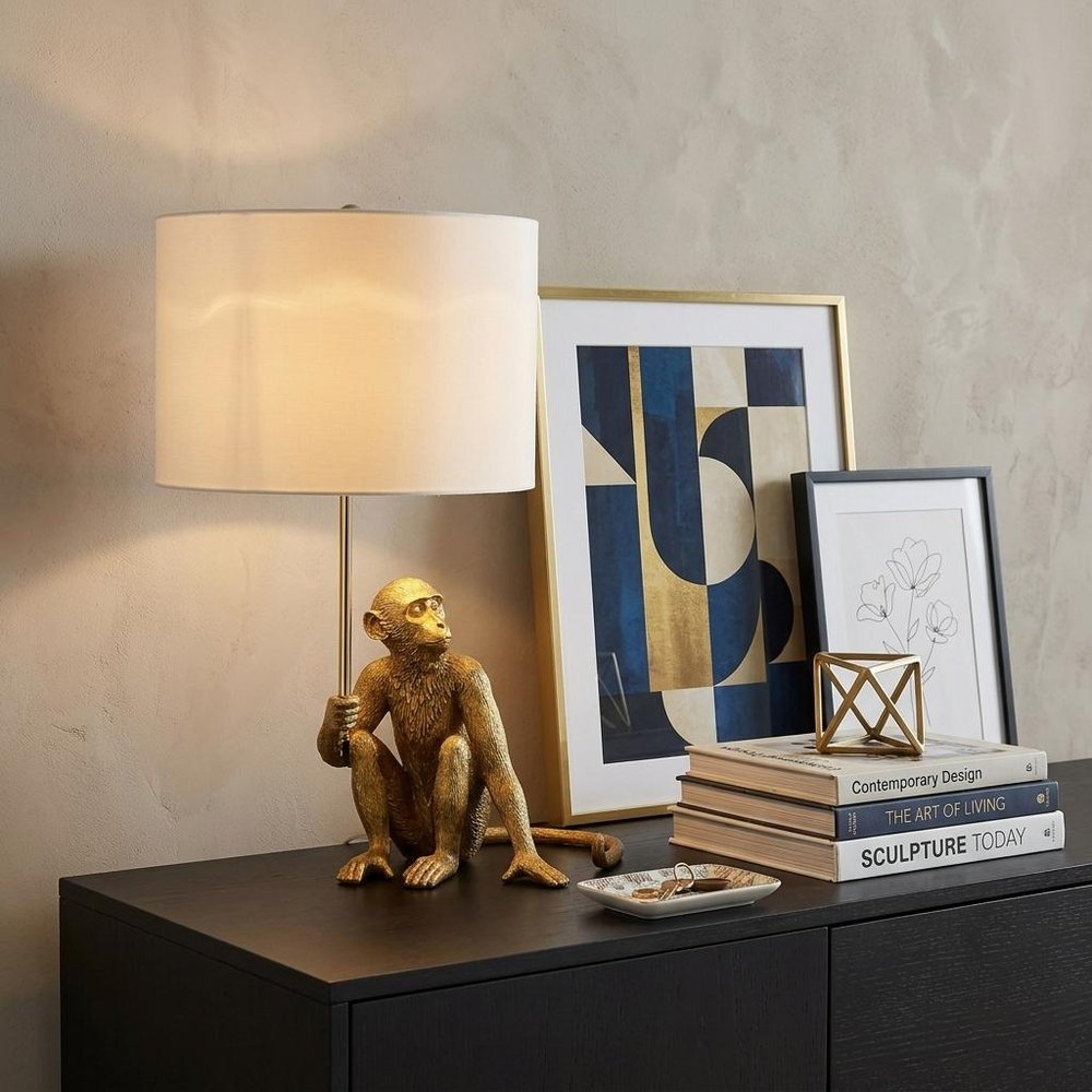 26" Antiqued Gold Sitting Monkey Table Lamp With White displayed on a tabletop in a furnished interior against a tan wall.