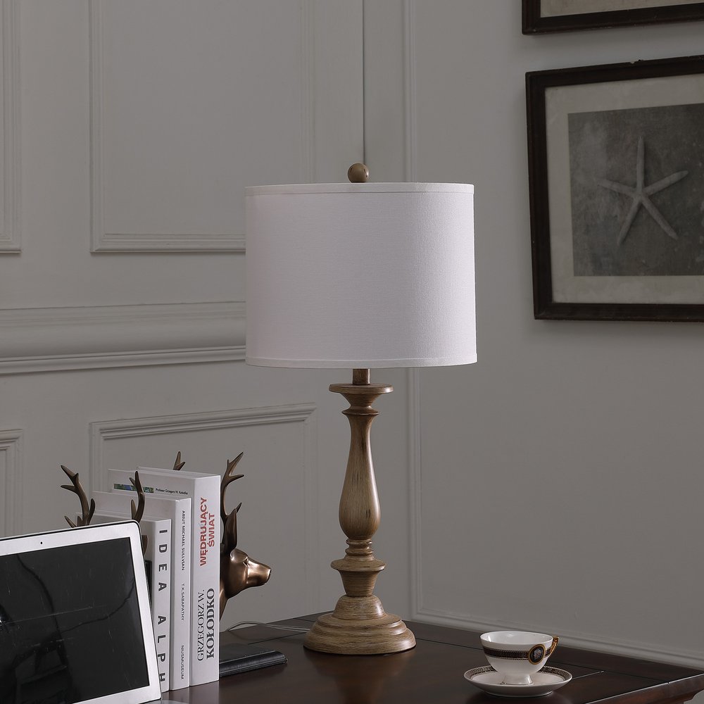 28" Rustic Taupe Cream Candlestick Table Lamp With White Shade displayed on a tabletop in a furnished interior against a gray wall.