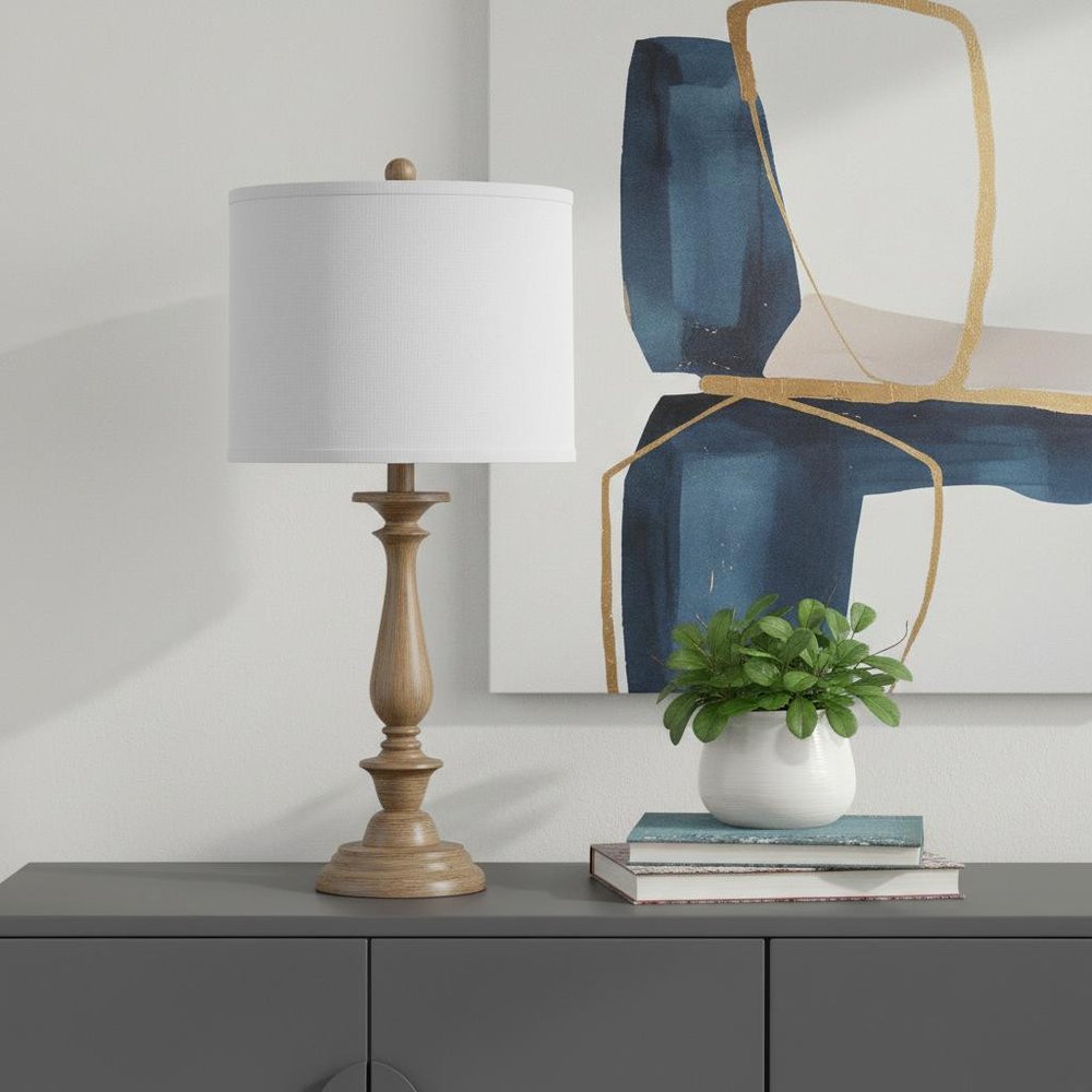 28" Rustic Taupe Cream Candlestick Table Lamp With White Shade displayed on a tabletop in a furnished interior against a light gray wall.