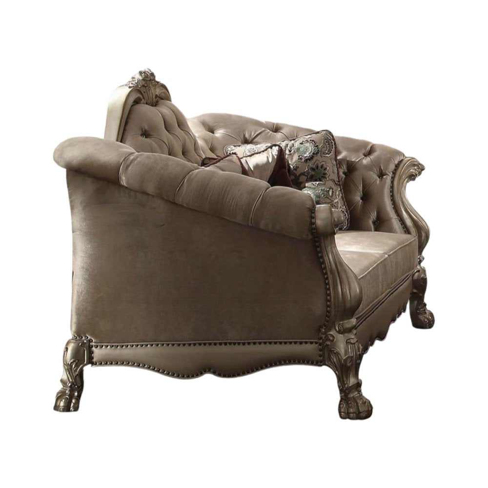 A bone-colored velvet loveseat with tufted back and ornate carved wooden legs, featuring two decorative toss pillows on a white background.
