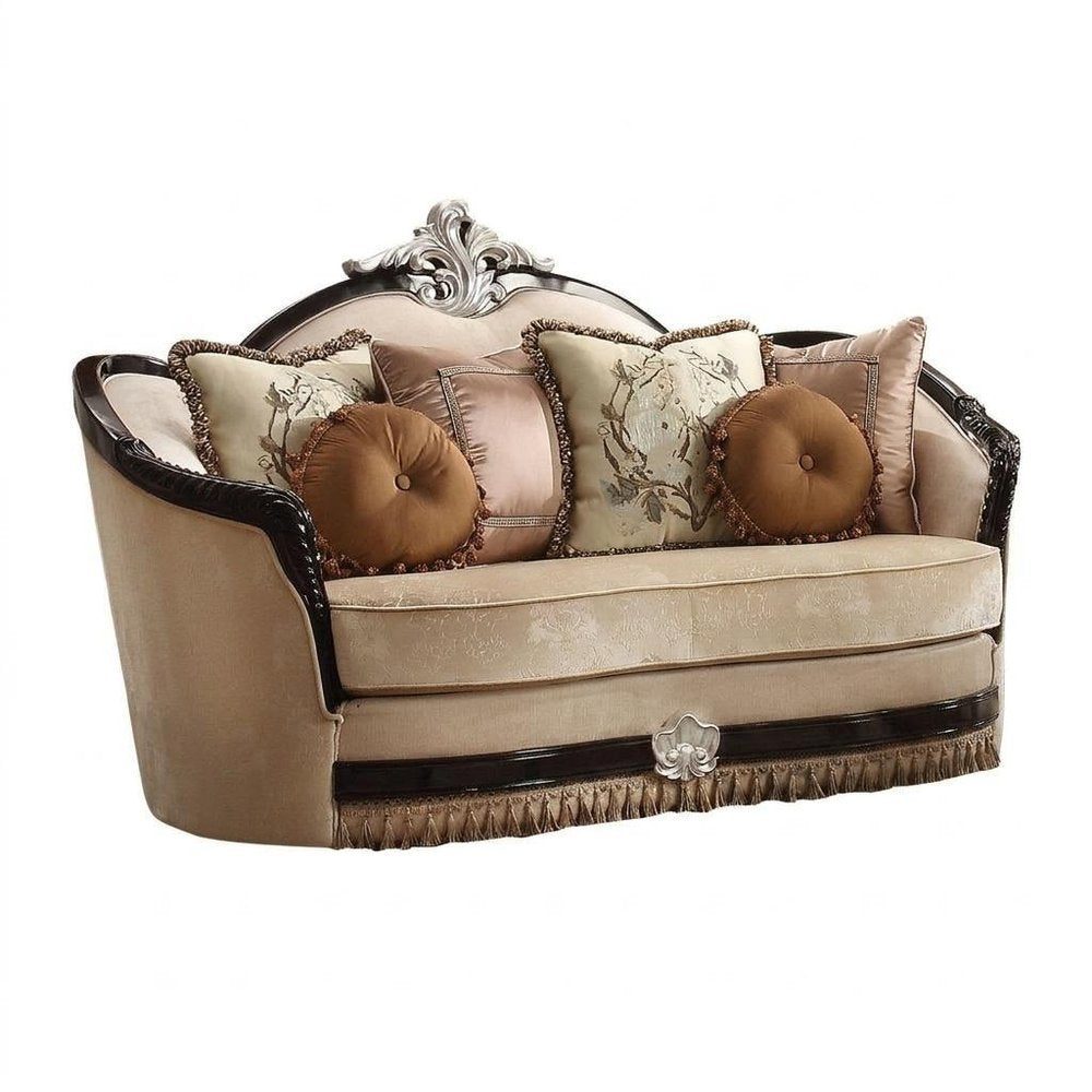 Tan velvet curved loveseat with decorative pillows and ornate dark wood trim on a white background.