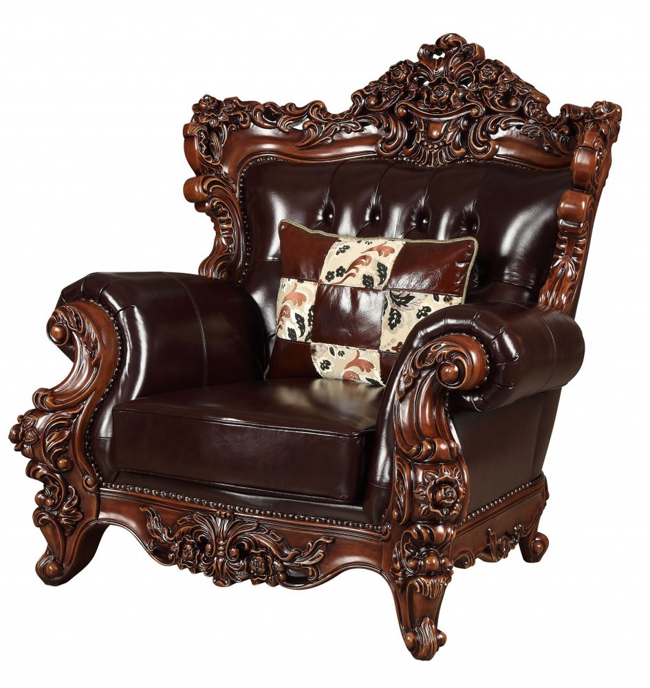 Espresso faux leather tufted wingback chair with ornate wood trim and a patchwork toss pillow on a white background.