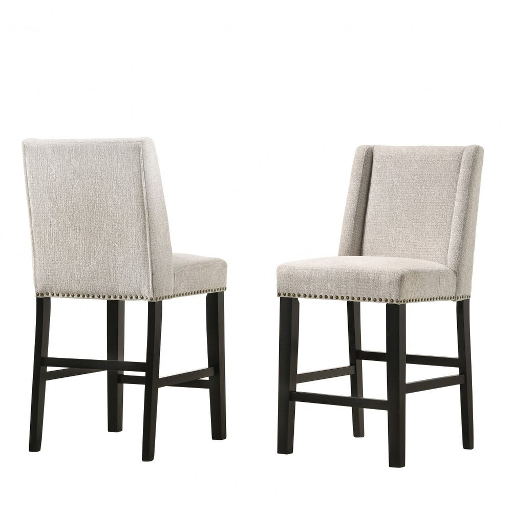 Two fawn upholstered bar chairs with espresso iron legs and nailhead trim on a white background.