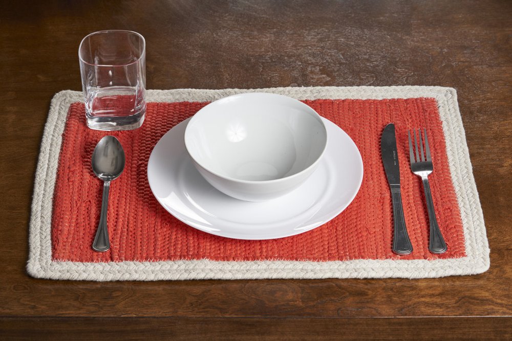 19" Set of Four Orange And Natural Solid With Border Cotton Placemats styled in a furnished interior with a dark brown wall on a dark wood floor.