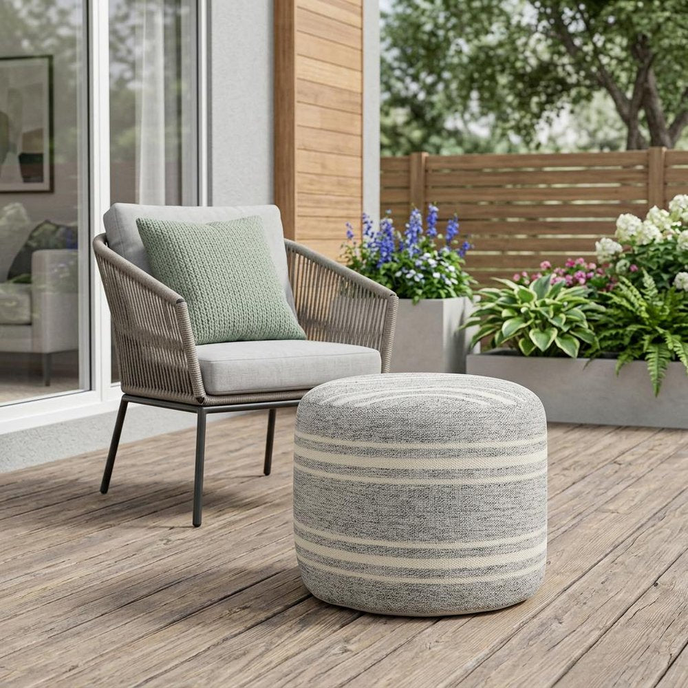 18" Gray Polyester Round Striped Indoor Outdoor Pouf Ottoman shown outdoors on a patio with greenery.
