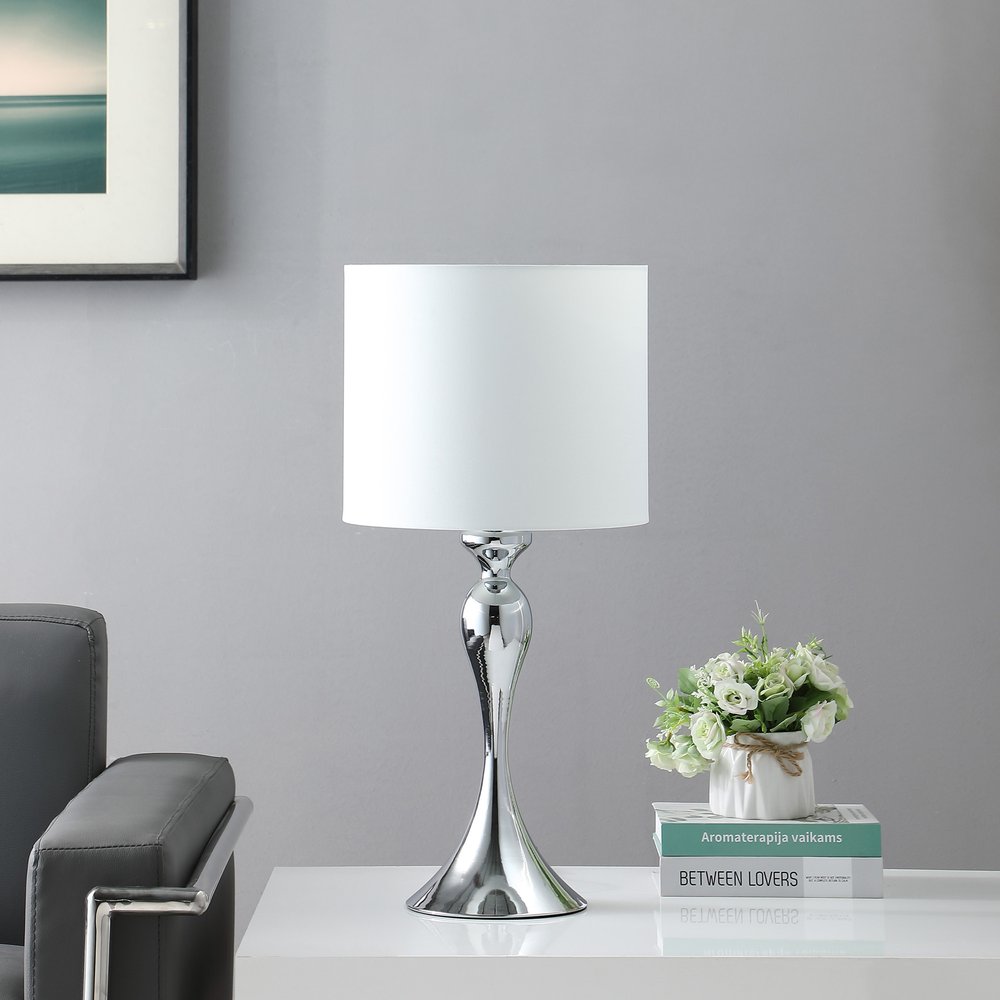 25" Silver Sleek Table Lamp With Off White Drum Shade displayed on a tabletop in a furnished interior against a light gray wall in off-white.