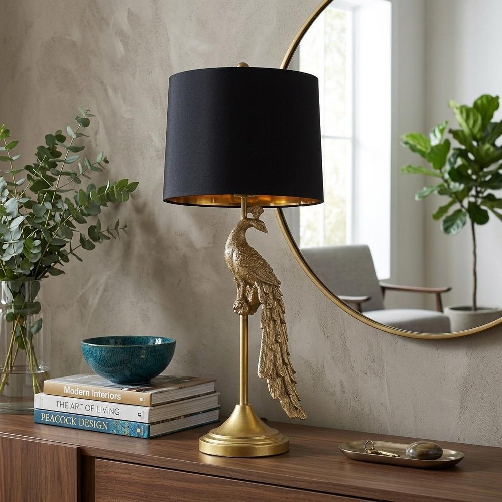 29" Gold Peacock Table Lamp With Black Drum Shade displayed on a dark wood tabletop in a furnished interior against a tan wall.