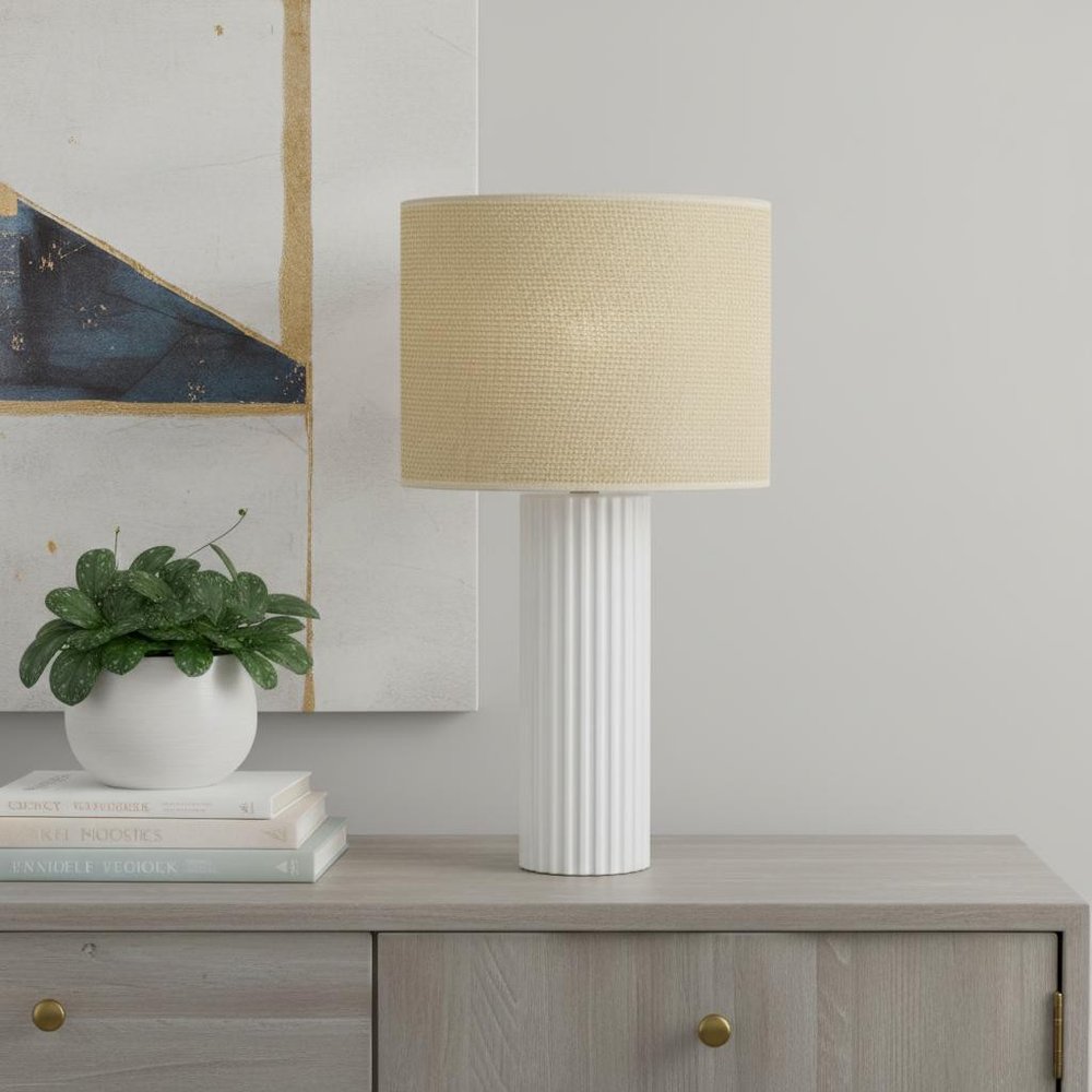 24" White Ceramic Cylinder Table Lamp With Beige Drum Shade displayed on a tabletop in a furnished interior against a light gray wall.