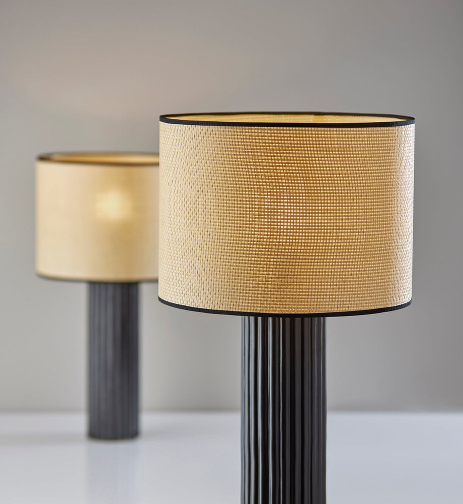 29" Black Ceramic Cylinder Table Lamp With Beige Drum Shade displayed on a tabletop in a furnished interior against a gray wall.