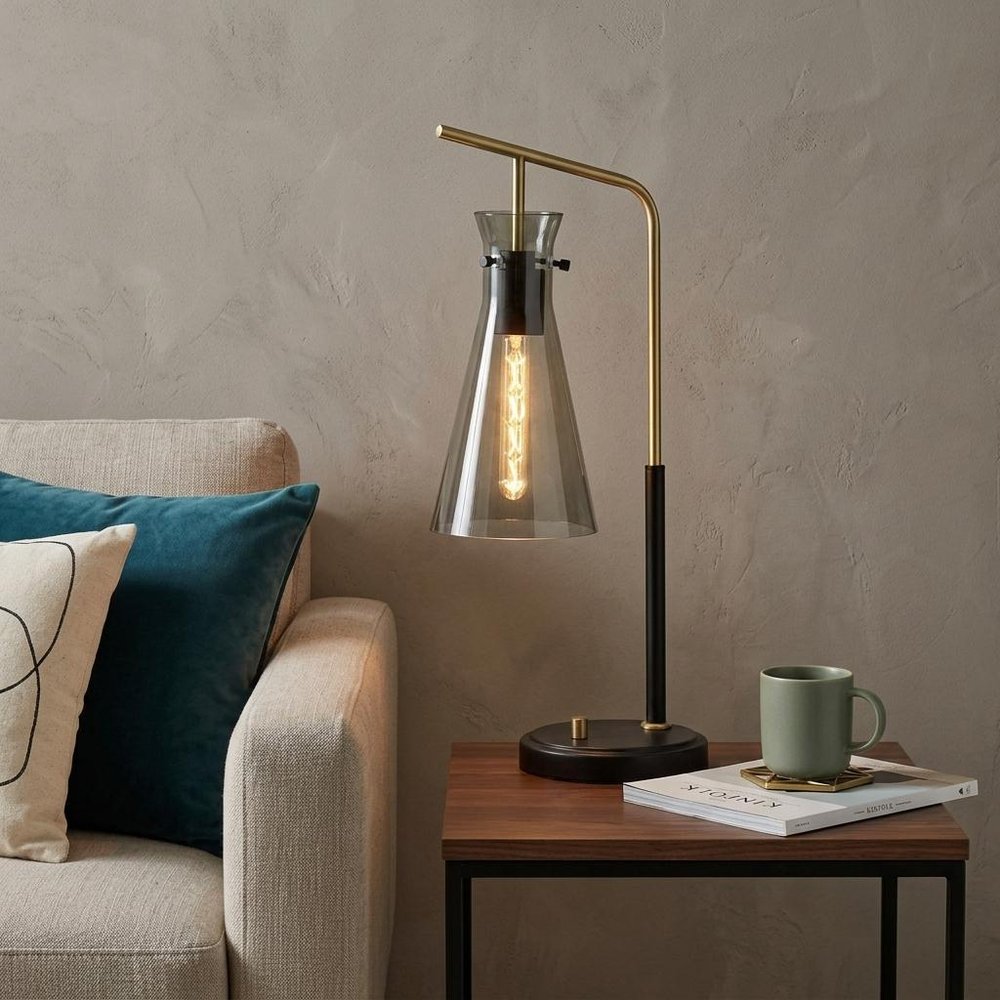 24" Black and Gold Metal Desk Lamp With Light Gray Cone Shade styled in a furnished interior with a tan wall on a dark wood floor.