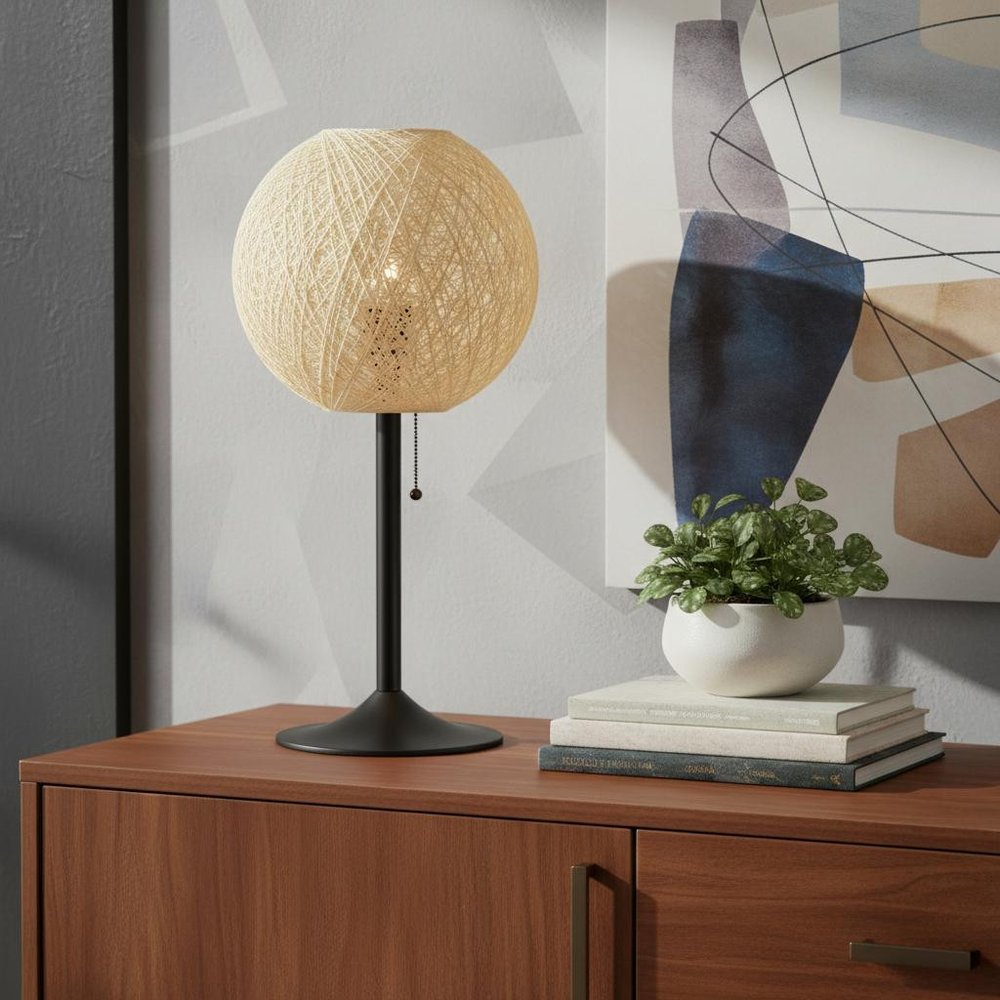 24" Antiqued Bronze Metal Candlestick Table Lamp With Off White Globe Shade displayed on a dark wood tabletop in a furnished interior against a light gray wall in off-white metal.
