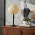 24" Antiqued Bronze Metal Candlestick Table Lamp With Off White Globe Shade displayed on a dark wood tabletop in a furnished interior against a light gray wall in off-white metal.