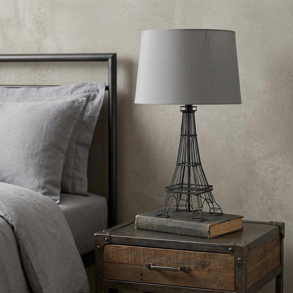25" Black Acrylic Paris Desk Table Lamp With Gray Drum Shade displayed on a dark wood tabletop in a furnished interior against a light gray wall.