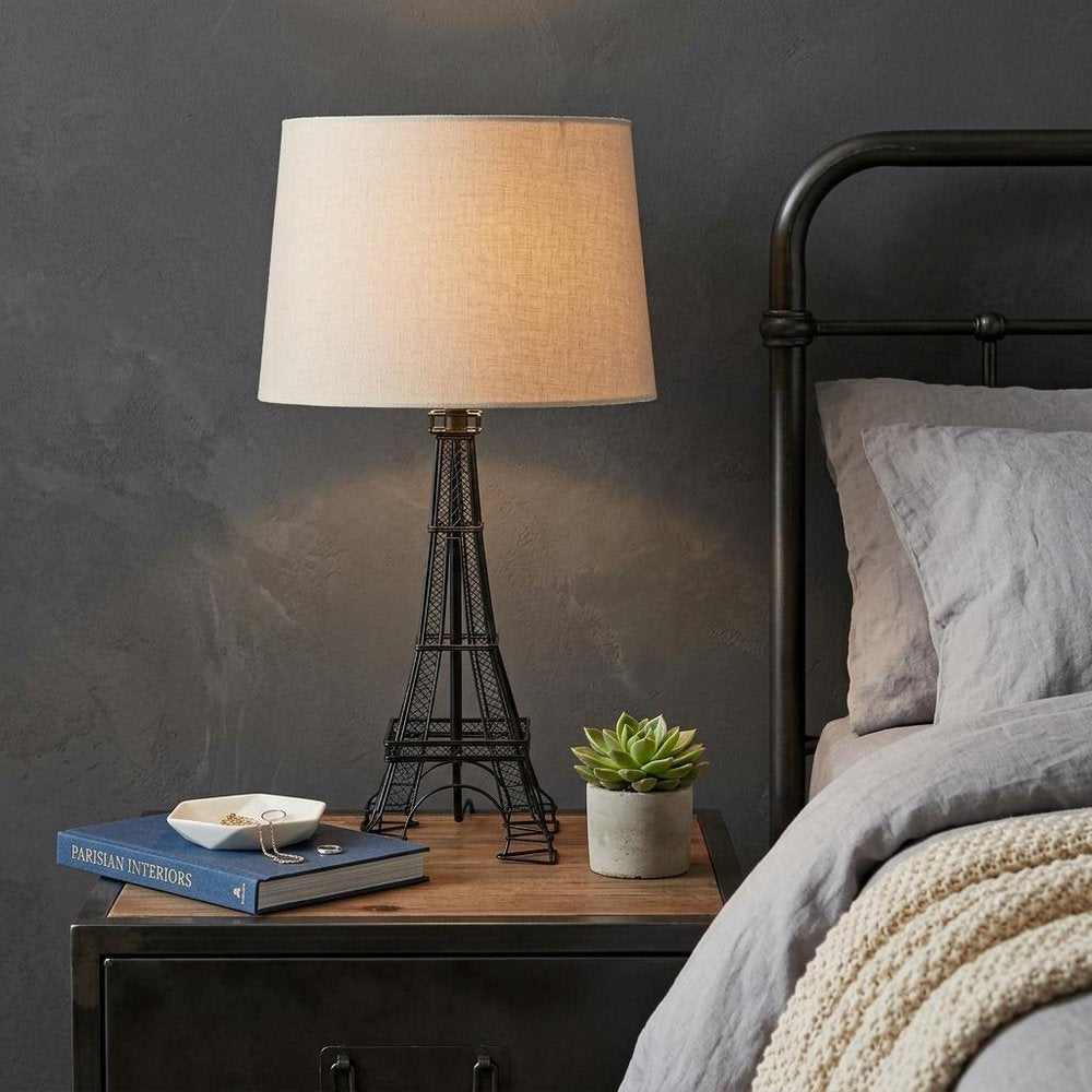 25" Black Acrylic Paris Desk Table Lamp With White Drum Shade displayed on a tabletop in a furnished interior against a dark wall.