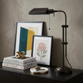 26" Bronze Metal Adjustable Table Lamp With Bronze Rectangular Shade displayed on a tabletop in a furnished interior against a tan wall.
