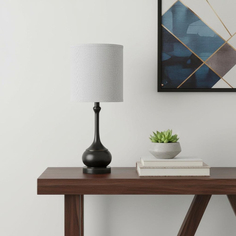 25" Blackened Bronze Metal Round Table Lamp With Off White Drum Shade shown outdoors on an outdoor setting in off-white metal.