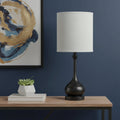 25" Blackened Bronze Metal Round Table Lamp With Off White Drum Shade shown outdoors on an outdoor setting.