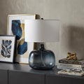 24" Dark Blue Glass Table Lamp With White Novelty Shade displayed on a tabletop in a furnished interior against a light gray wall.