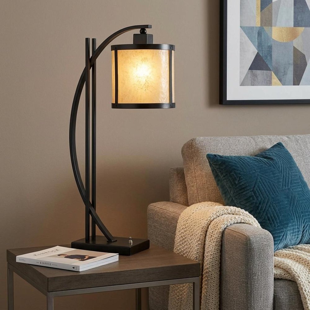 26" Black Metal Lantern Table Lamp With White Drum Shade displayed on a dark wood tabletop in a furnished interior against a tan wall.
