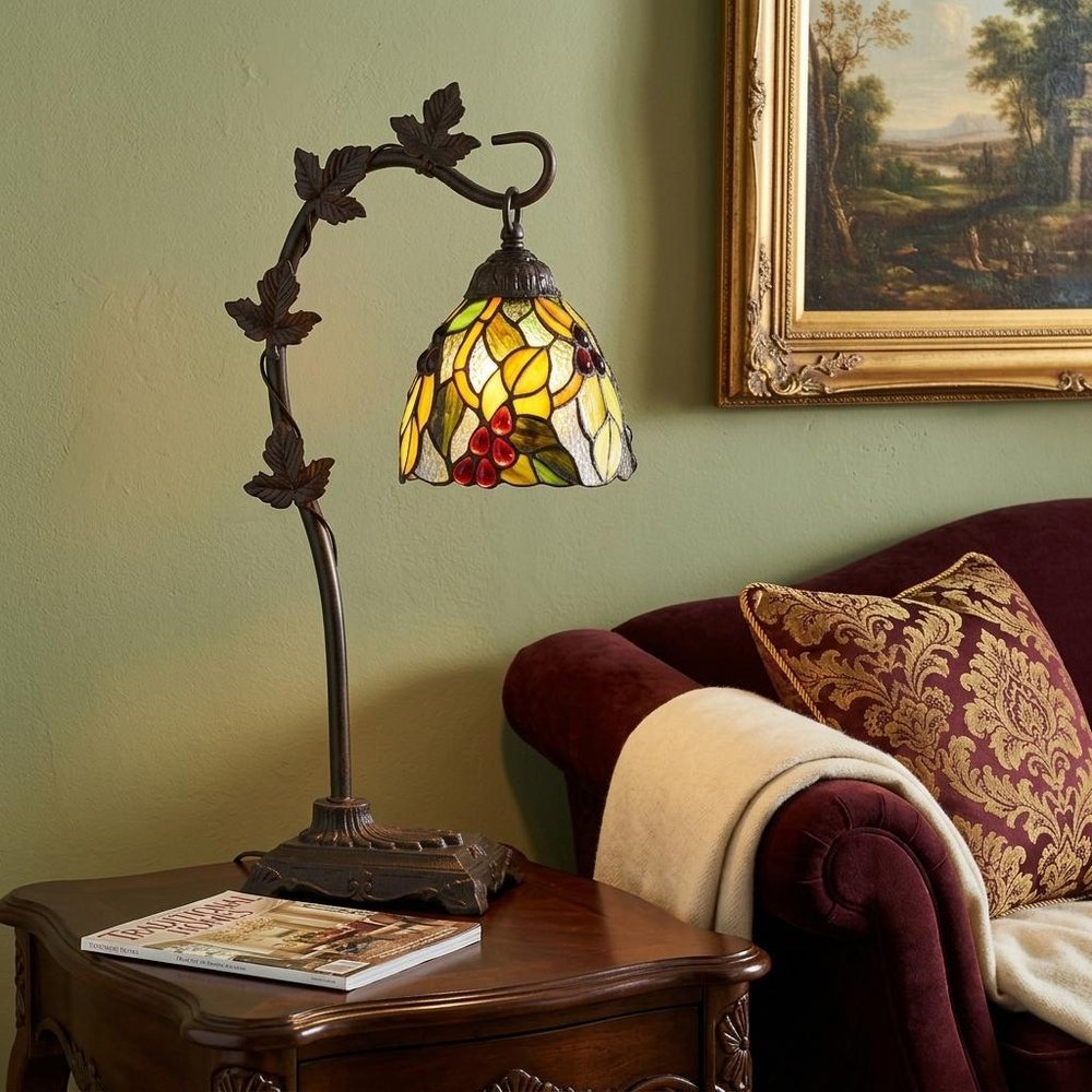 24" Bronze Metal Tiffany Style Table Lamp With Hanging Stained Glass Shade displayed on a tabletop in a furnished interior against a gold wall.