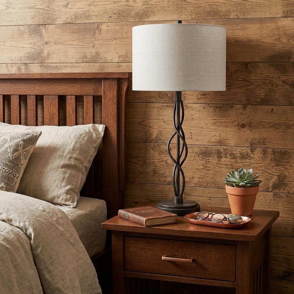 30" Black Metal Candlestick Table Lamp With Off White Drum Shade displayed on a dark wood tabletop in a furnished interior against a tan wall.