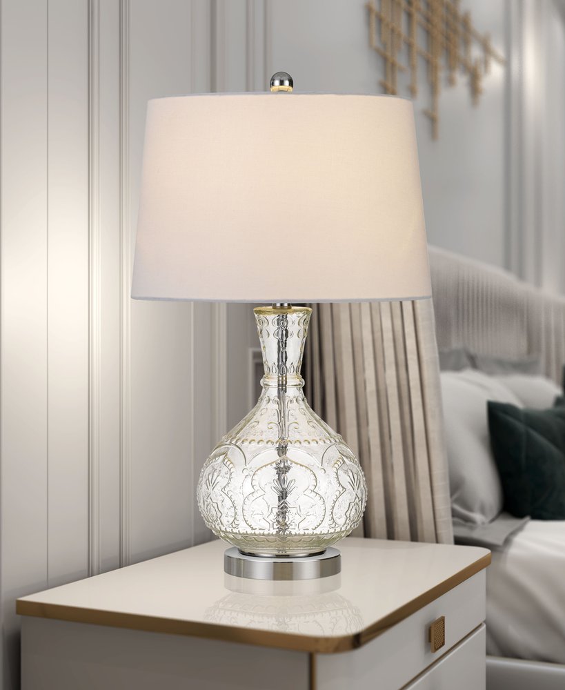 27" Clear Metal Round Table Lamp With White Shade displayed on a tabletop in a furnished interior against a light gray wall.
