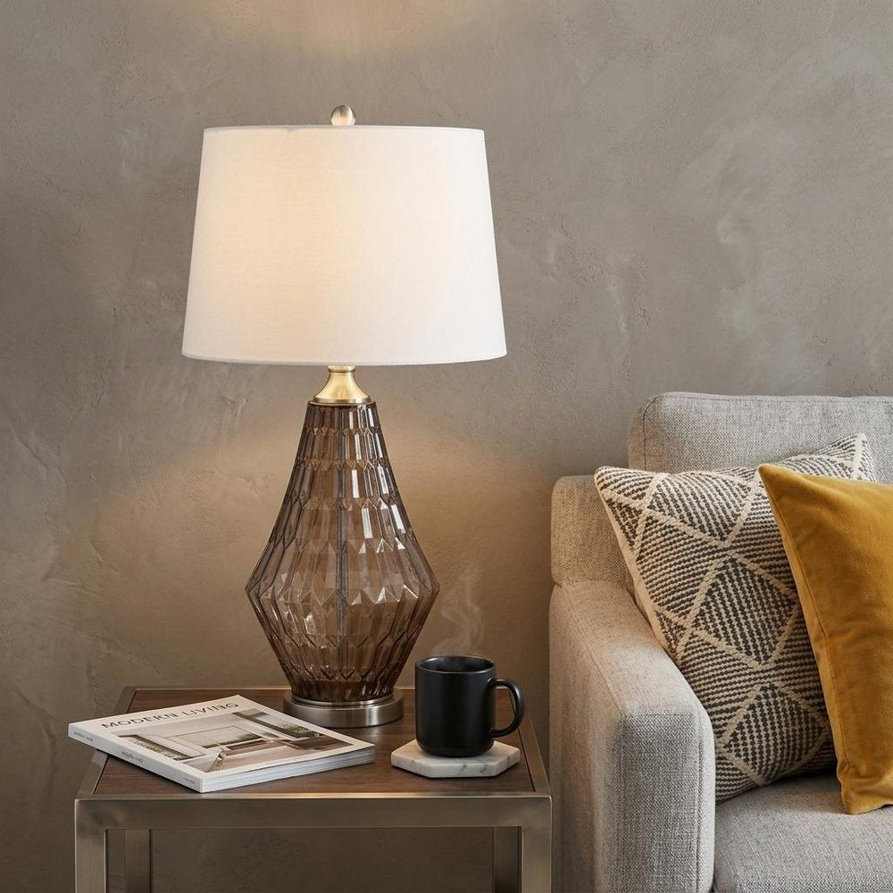 31" Gray Metal Geometric Table Lamp With Off White Empire Shade displayed on a dark wood tabletop in a furnished interior against a tan wall.