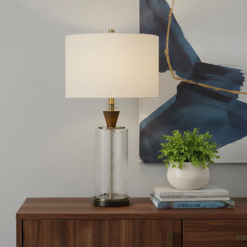 30" Clear Metal Table Lamp With White Empire Shade displayed on a dark wood tabletop in a furnished interior against a light gray wall.