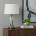 29" Clear Metal Table Lamp With White Empire Shade displayed on a dark wood tabletop in a furnished interior against a light gray wall.