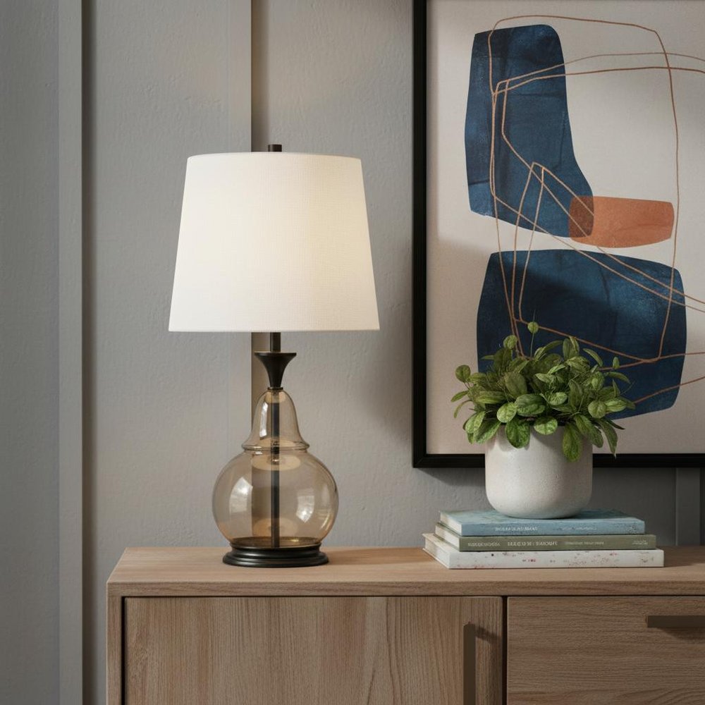 28" Clear Metal Table Lamp With White Empire Shade displayed on a dark wood tabletop in a furnished interior against a gray wall.