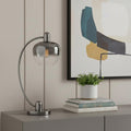 27" Gunmetal Metal Table Lamp With Silver Metallic Globe Shade displayed on a tabletop in a furnished interior against a tan wall.