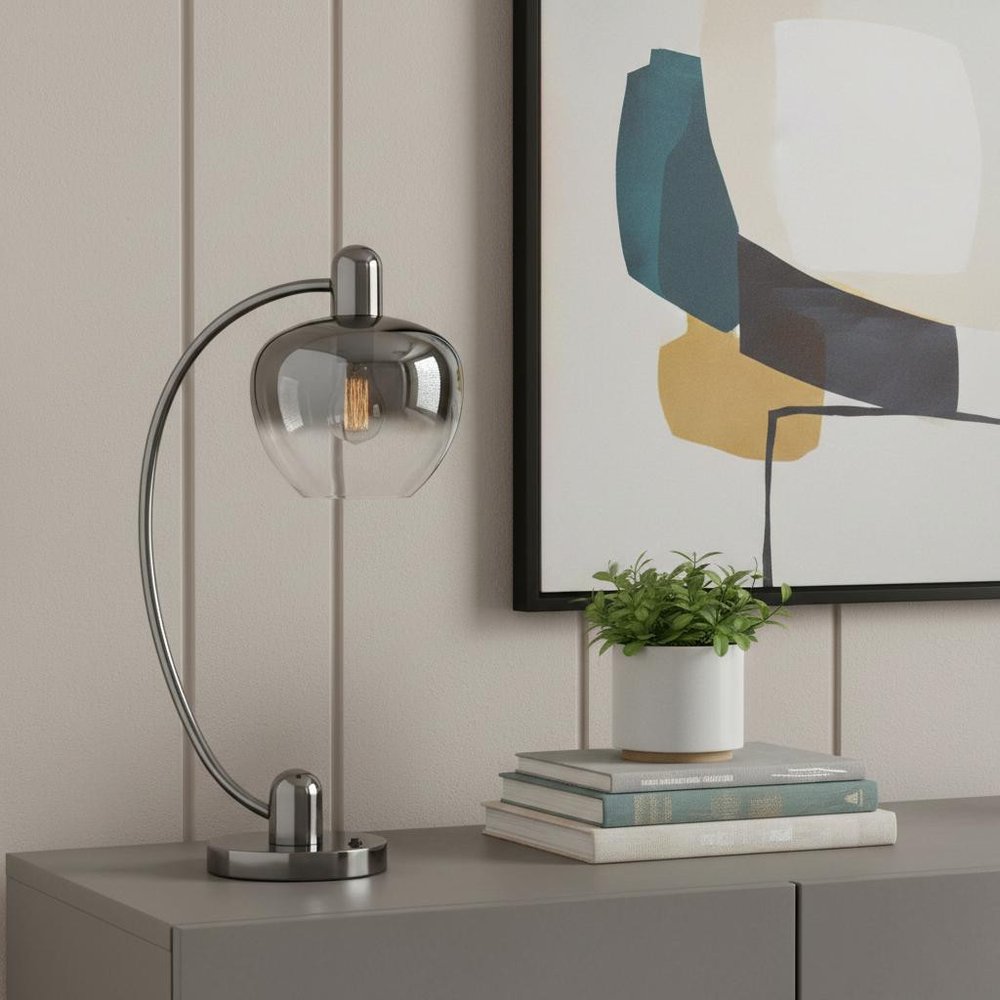 27" Gunmetal Metal Table Lamp With Silver Metallic Globe Shade displayed on a tabletop in a furnished interior against a tan wall.