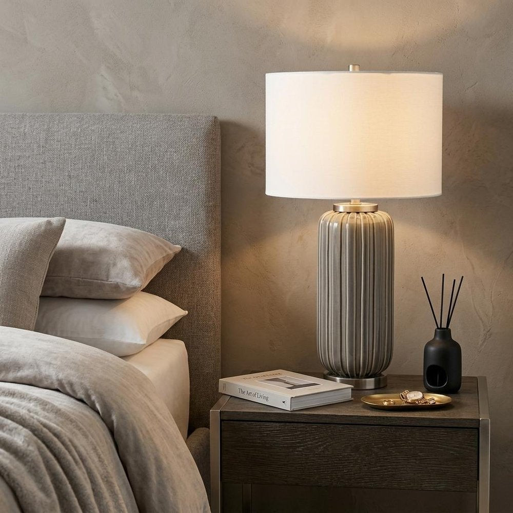 29" Gray Metal Cylinder Table Lamp With White Drum Shade displayed on a dark wood tabletop in a furnished interior against a tan wall.
