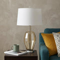 29" Nickel Metal Round Table Lamp With White Drum Shade displayed on a tabletop in a furnished interior against a tan wall in silver metal.