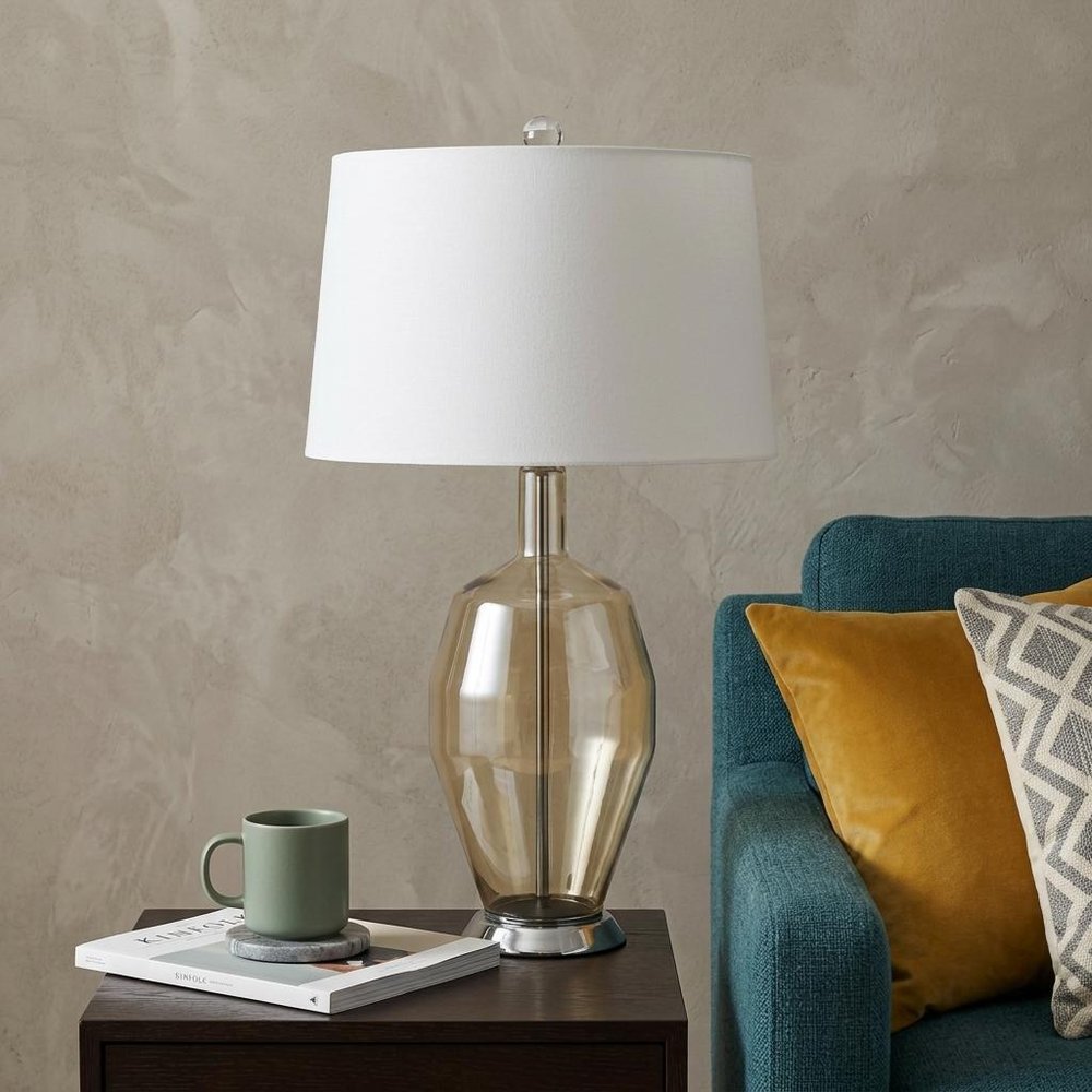 29" Nickel Metal Round Table Lamp With White Drum Shade displayed on a tabletop in a furnished interior against a tan wall in silver metal.
